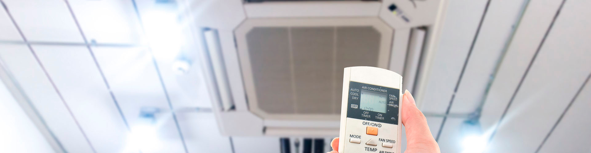Hand holding remote control to operate a ceiling-mounted cassette air conditioning unit