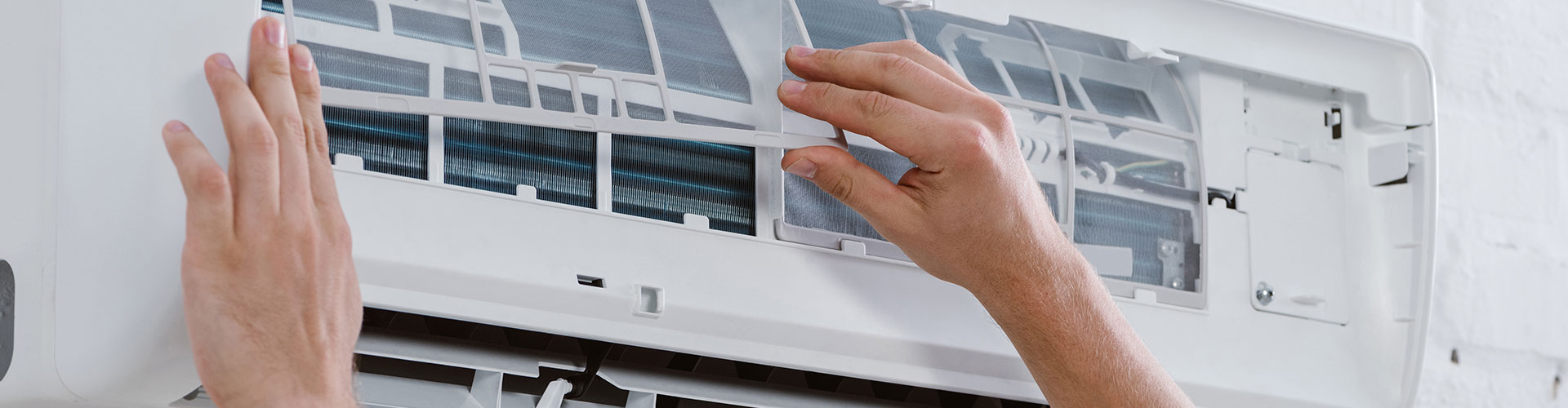 Hands installing a white mesh filter panel into an open wall-mounted air conditioning unit
