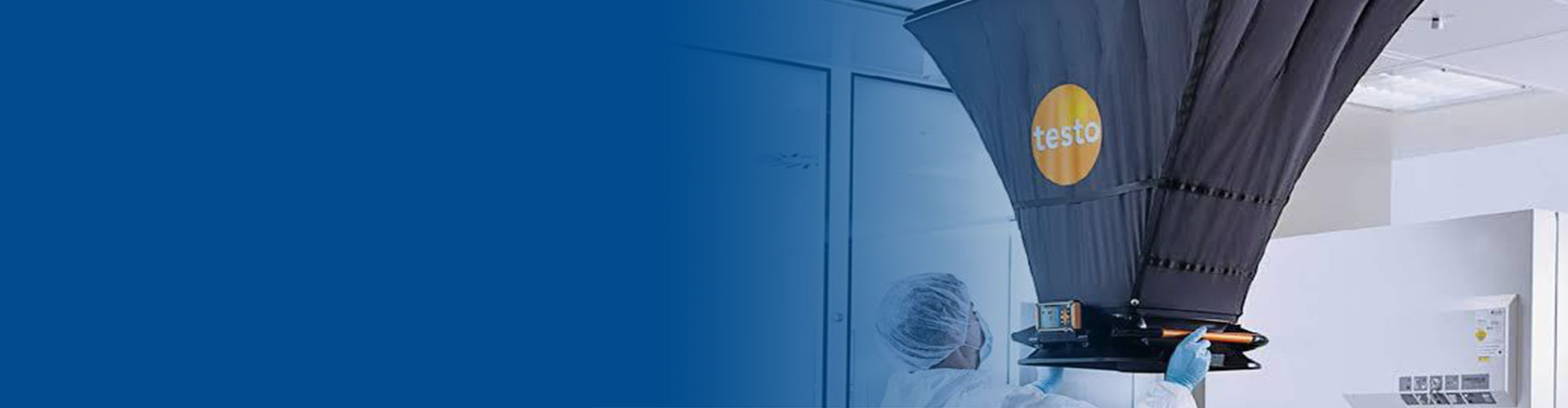 Cleanroom technician in protective suit performing air flow testing at a ceiling vent using a testo capture hood