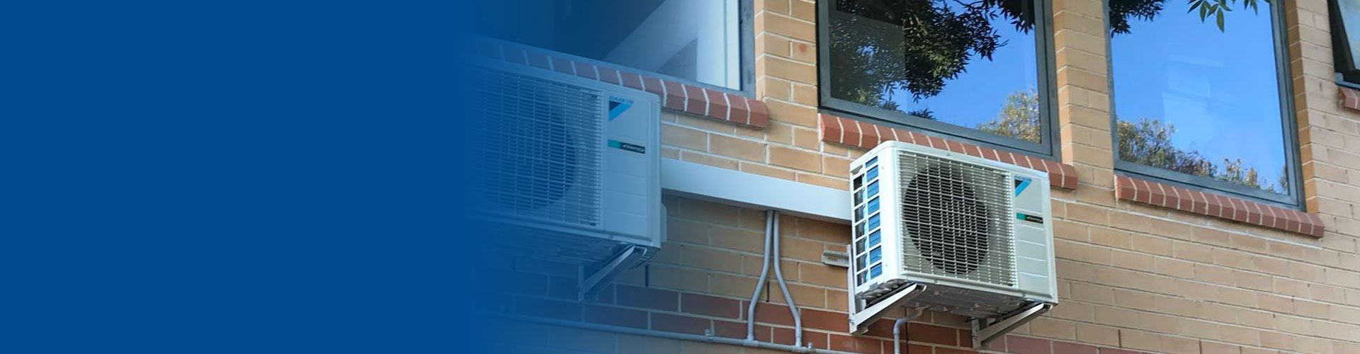 Two outdoor AC condenser units mounted on brick wall with copper piping, banner with blue overlay for text