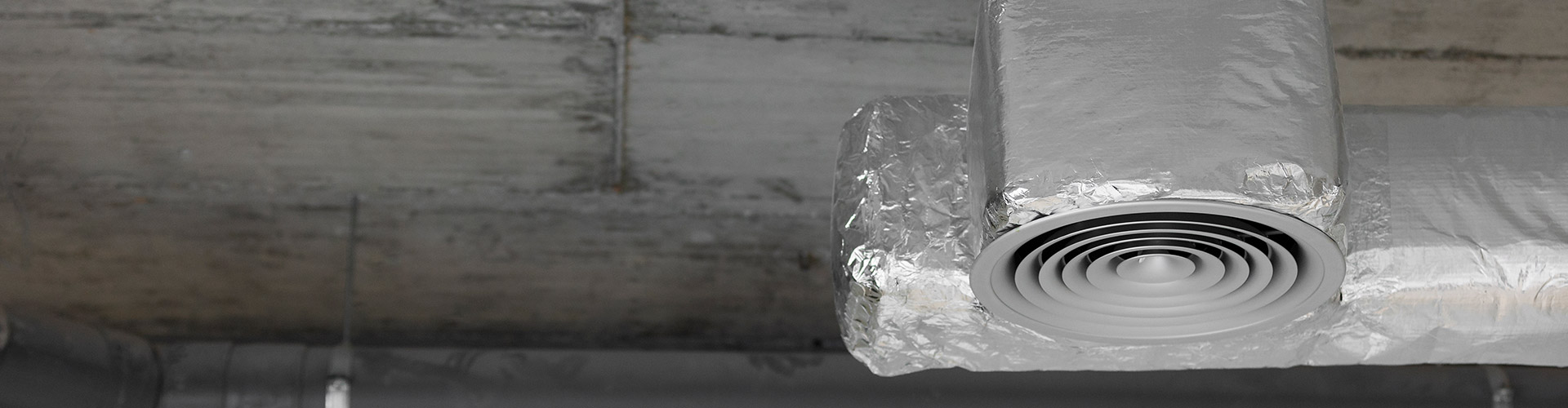 Foil-wrapped HVAC ductwork with round diffuser vent on exposed concrete ceiling
