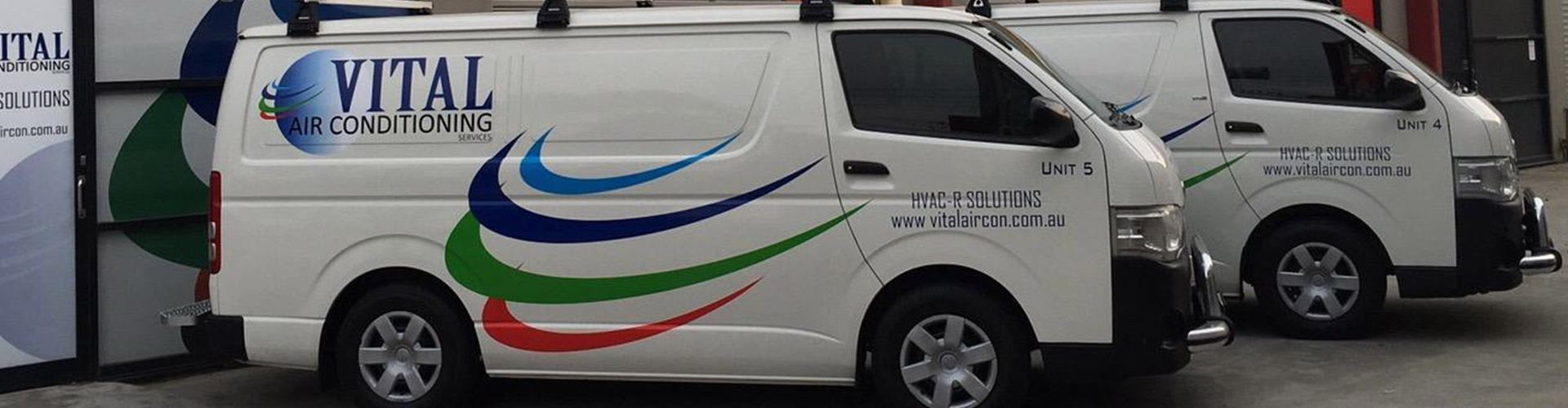 Two Vital Air Conditioning Services vans, Unit 4 and Unit 5, parked outside an HVAC-R service building