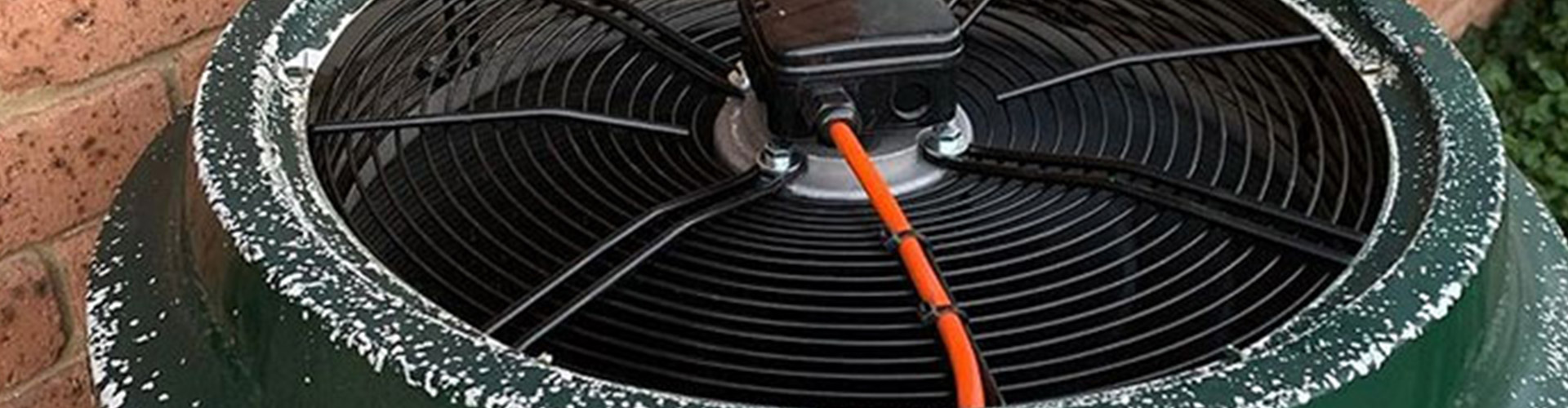 Top-down view of a corroded outdoor AC condenser fan with orange wiring against a brick wall