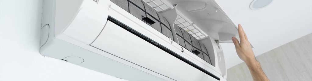 Hand opening the front panel of a white wall-mounted inverter air conditioning unit to reveal the filter
