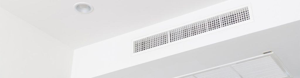 Ducted air conditioning vent and recessed light on a white ceiling corner