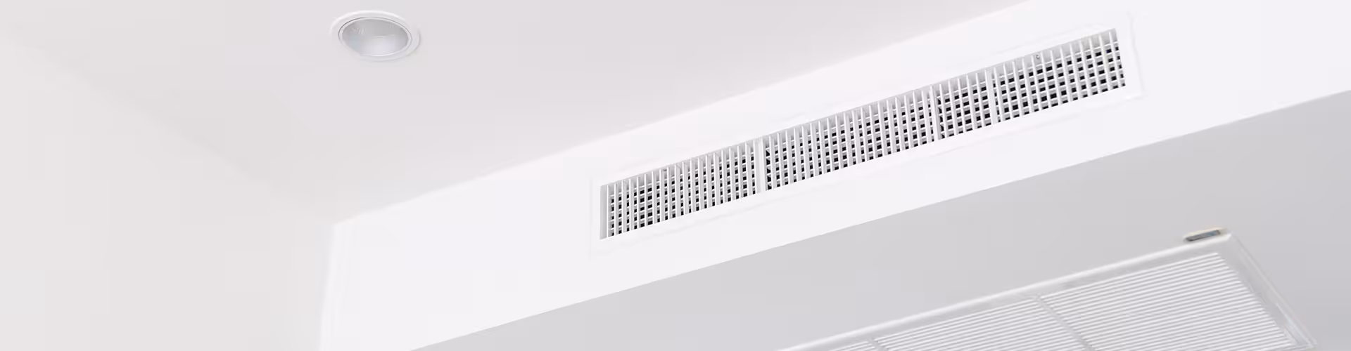 Ducted air conditioning vent and recessed light on a white ceiling corner