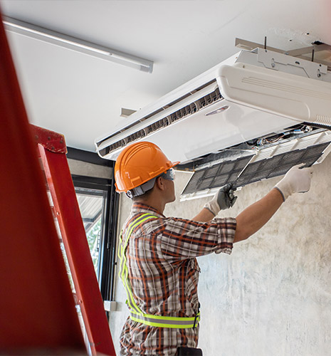Technician in orange hard hat repairing a wall-mounted air conditioning unit to improve air flow in your home