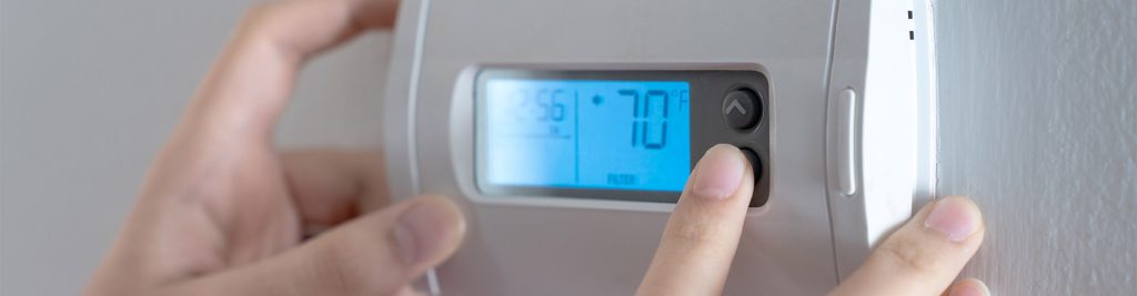 Hand adjusting a wall-mounted digital thermostat set to 70°F for energy-efficient air conditioning