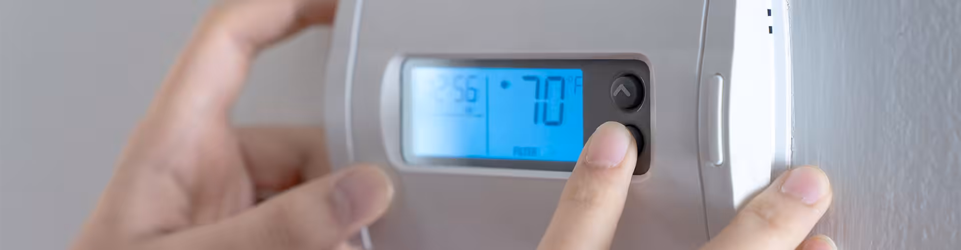 Hand adjusting a wall-mounted digital thermostat set to 70°F for energy-efficient air conditioning