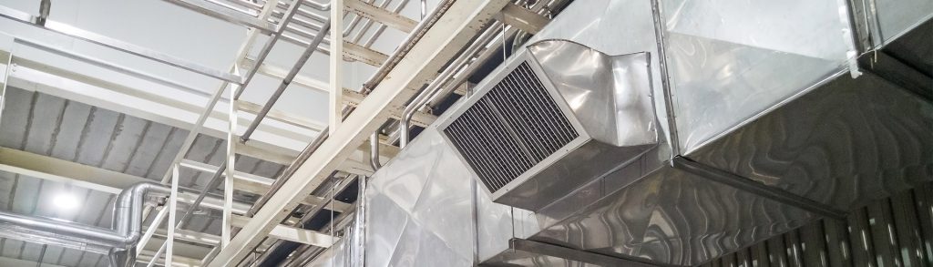 Industrial ceiling with metallic HVAC ductwork, vents, cable trays, and pipes overhead