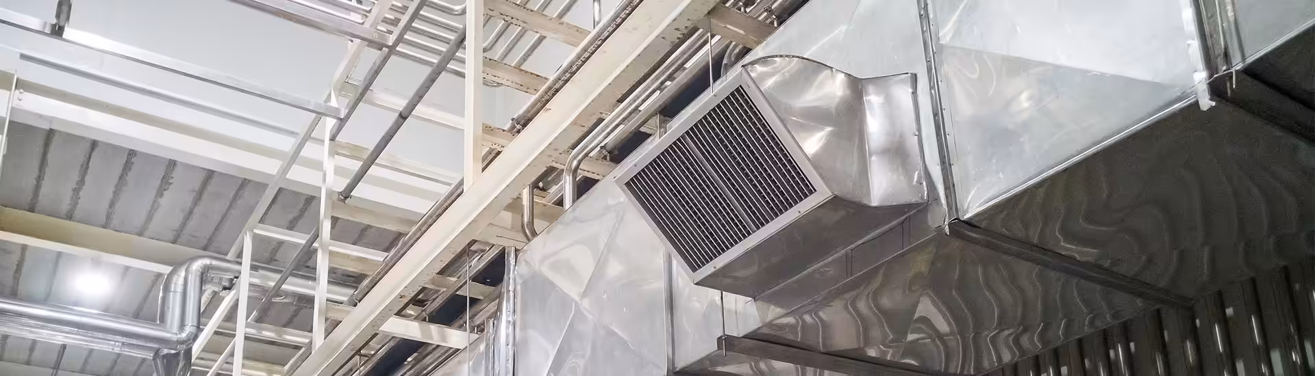 Industrial ceiling with metallic HVAC ductwork, vents, cable trays, and pipes overhead
