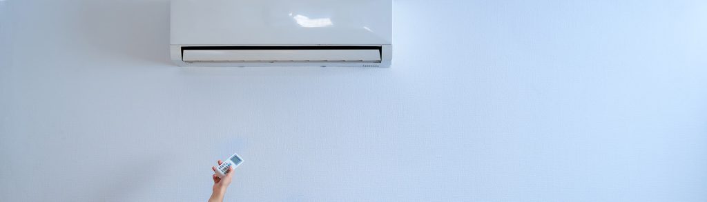 Wall-mounted split air conditioning unit being controlled with a white remote, comparing Daikin vs. Fujitsu systems