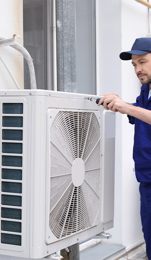 Technician repairing a ductless air conditioning condenser unit mounted on an exterior wall
