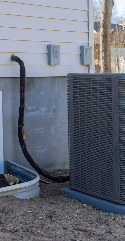 Outdoor HVAC condenser unit on concrete pad beside house with refrigerant line and electrical meter boxes