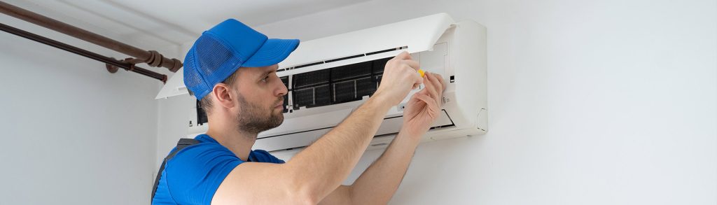 Technician repairing a ductless mini-split air conditioning unit with a screwdriver, filter panel open