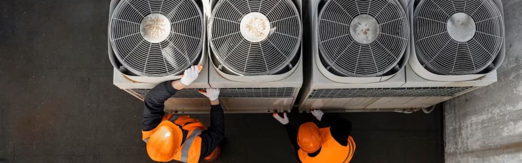 Technicians in safety gear performing maintenance on rooftop air conditioning system condenser units