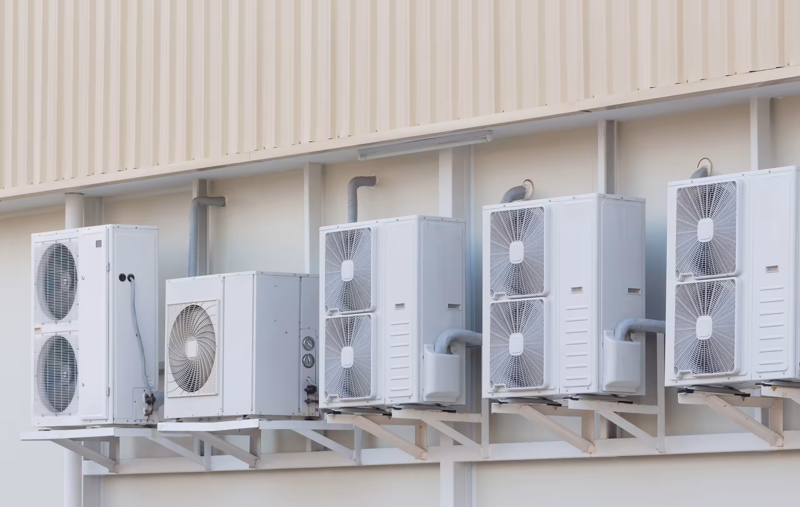 Row of six external air conditioning condenser units mounted on brackets outside a building's exterior wall