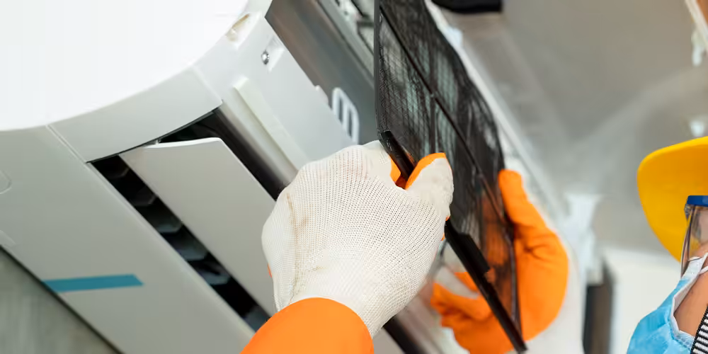 Technician removing a dusty filter mesh from a white wall-mounted split air conditioning unit