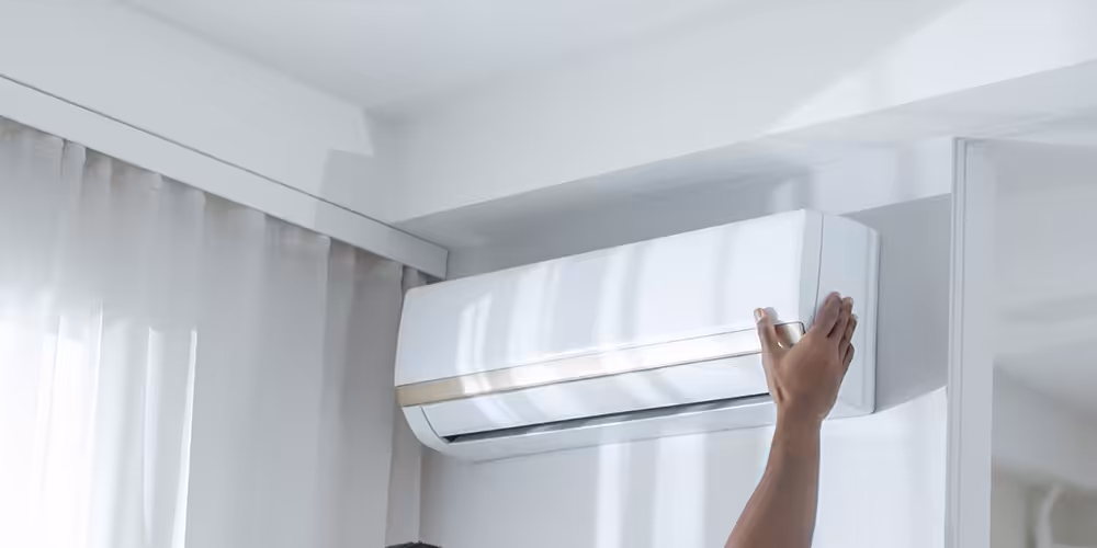 Technician's hand repairing a wall-mounted air conditioning unit near a ceiling corner