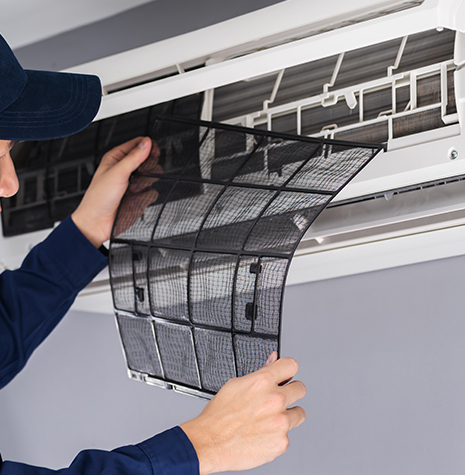 Technician removing a mesh air filter from a white wall-mounted split air conditioning unit for maintenance