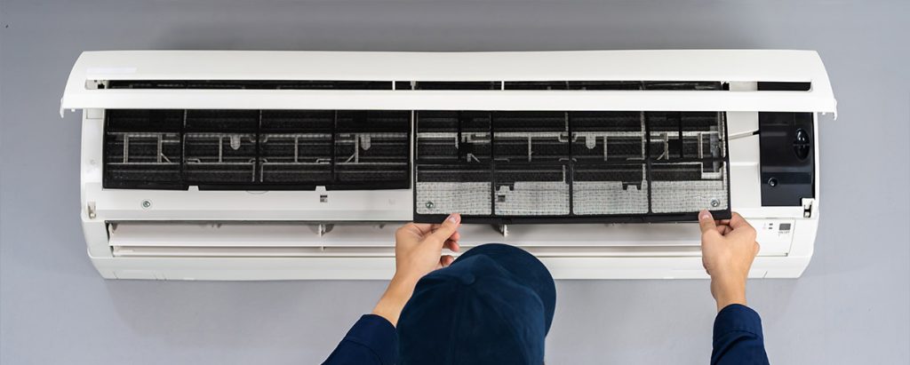 Person removing a filter panel from a wall-mounted air conditioning unit during maintenance