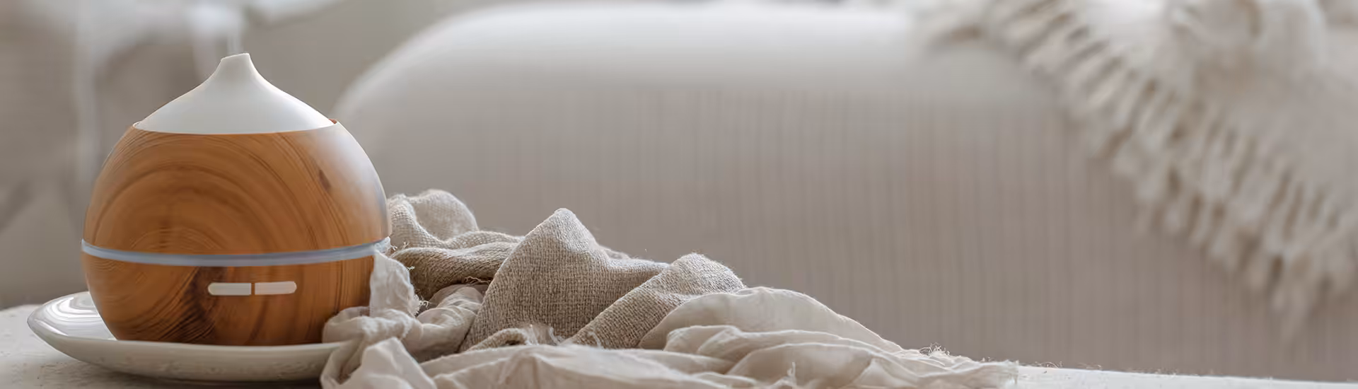 Wood-grain essential oil diffuser on a plate beside a linen cloth in a cozy living room, supporting indoor air quality