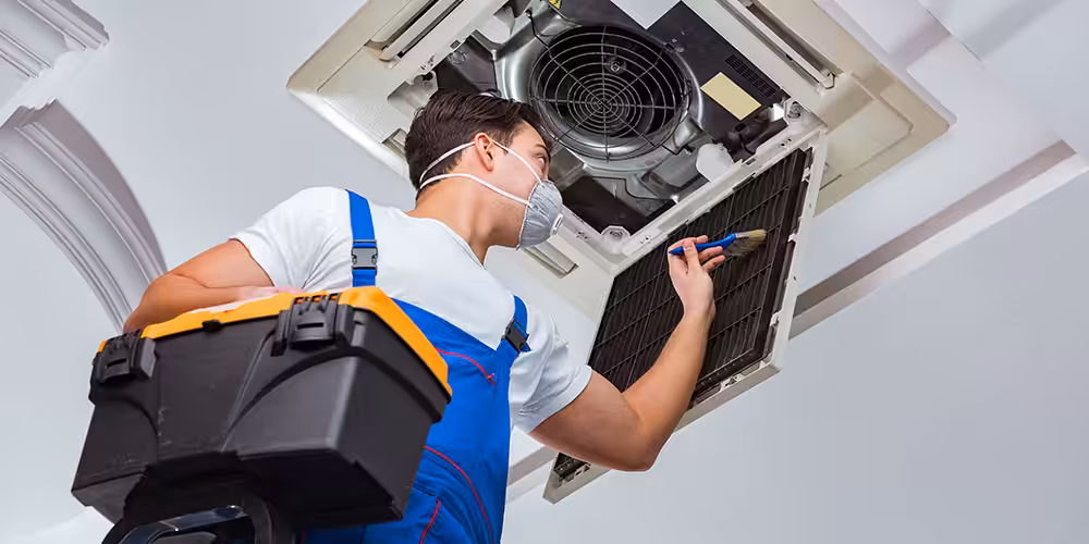 Aircon repairer cleaning the filter panel of a ceiling-mounted air conditioning unit