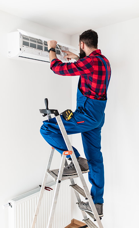 Aircon repairer on a ladder adjusting the front panel and vents of a wall-mounted air conditioning unit