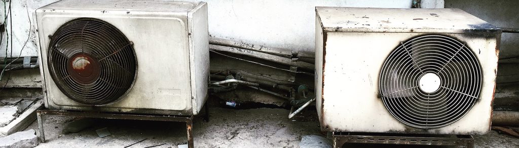 Rusty outdoor air conditioning compressor units with corroded copper piping showing anti-rust treatment need