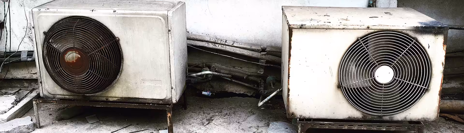 Rusty outdoor air conditioning compressor units with corroded copper piping showing anti-rust treatment need
