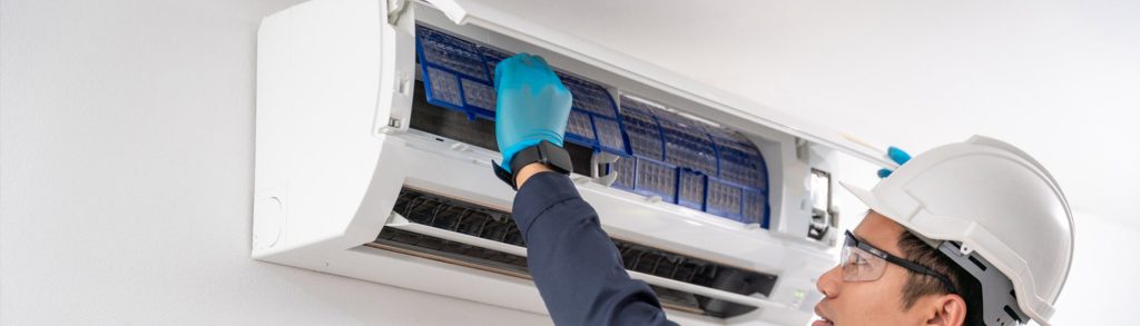Technician removing a blue mesh air filter from an open wall-mounted split air conditioning unit
