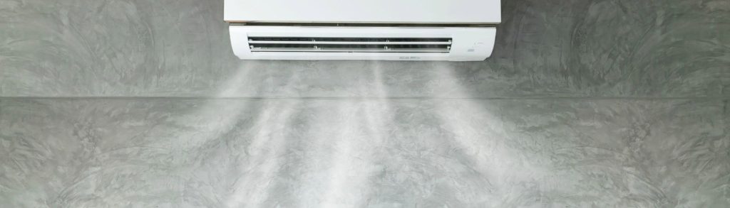 Wall-mounted split air conditioner blowing cool air for indoor humidity control on a concrete wall