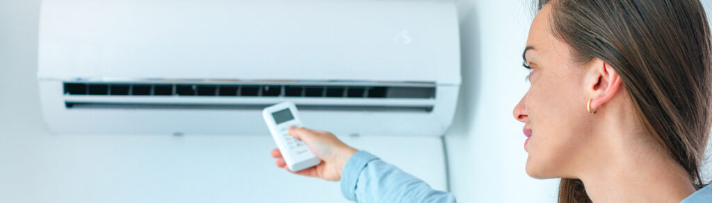 Woman pointing a remote at a wall-mounted AC unit that stops working