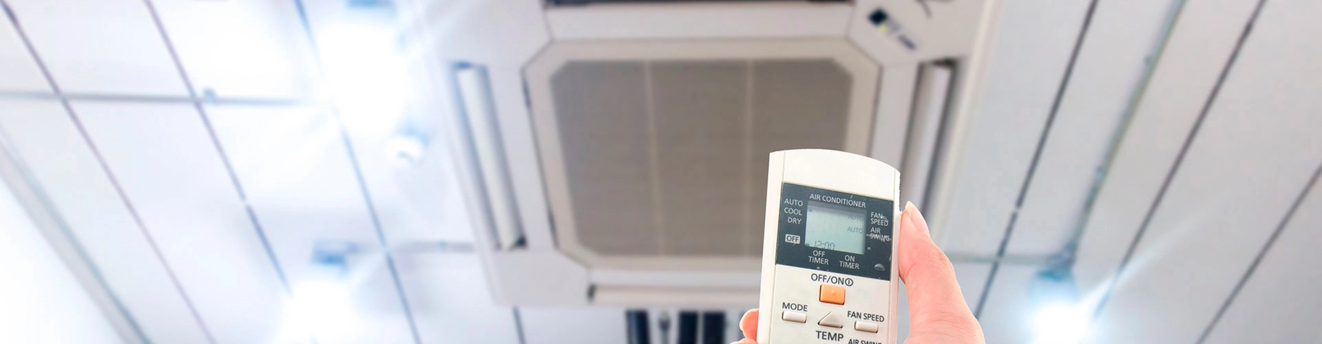 Hand holding a remote control to adjust a ceiling-mounted cassette air conditioning unit
