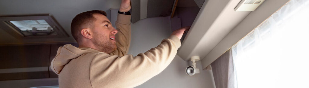 Man inspecting an overhead ceiling vent inside a vehicle to check weak AC airflow