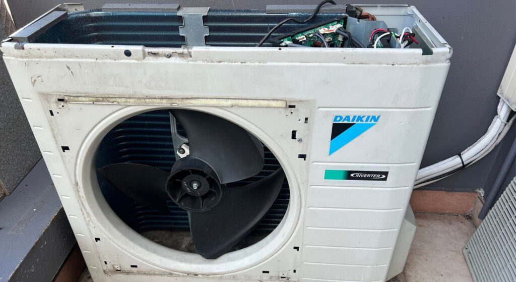 Daikin Inverter air conditioning condenser with cover removed, showing fan, coils, and wiring needing service