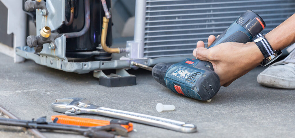 Technician using a cordless drill to service an outdoor air conditioning condenser unit