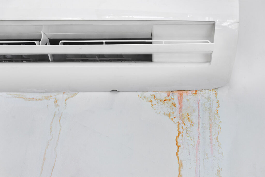 White air conditioner unit with rust-colored water stains leaking down the wall below it