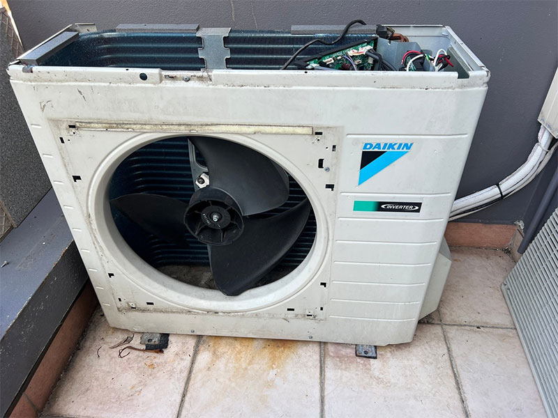 Daikin Inverter outdoor condenser unit with front panel removed, exposing fan blades, coil, and wiring